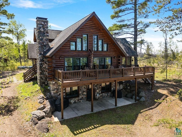 back of house with log exterior, a chimney, a deck, a patio area, and stone siding