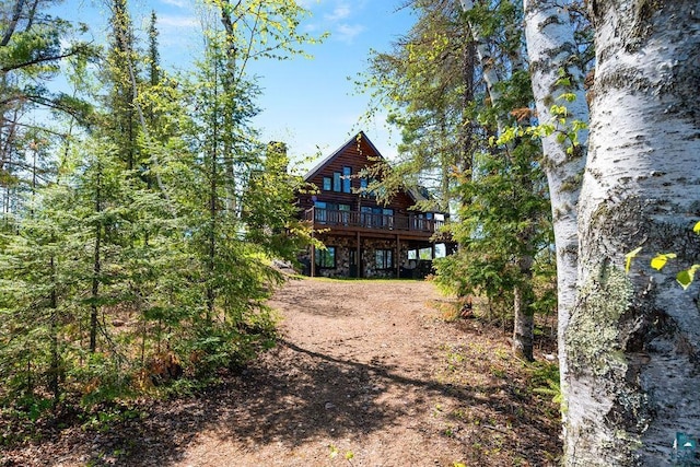 back of property with log siding, stone siding, a wooden deck, and dirt driveway