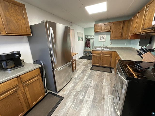 kitchen featuring light countertops, light wood-style floors, brown cabinetry, stainless steel appliances, and a sink