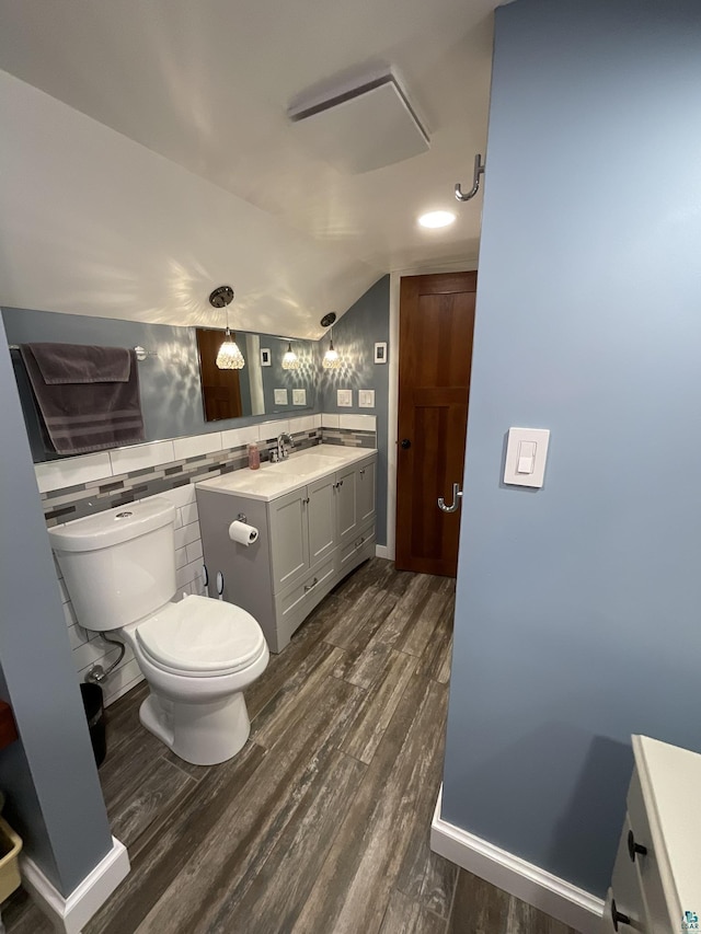 bathroom featuring tile walls, toilet, vaulted ceiling, wood finished floors, and vanity