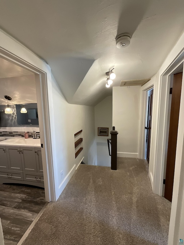 hallway featuring visible vents, lofted ceiling, an upstairs landing, dark colored carpet, and a sink