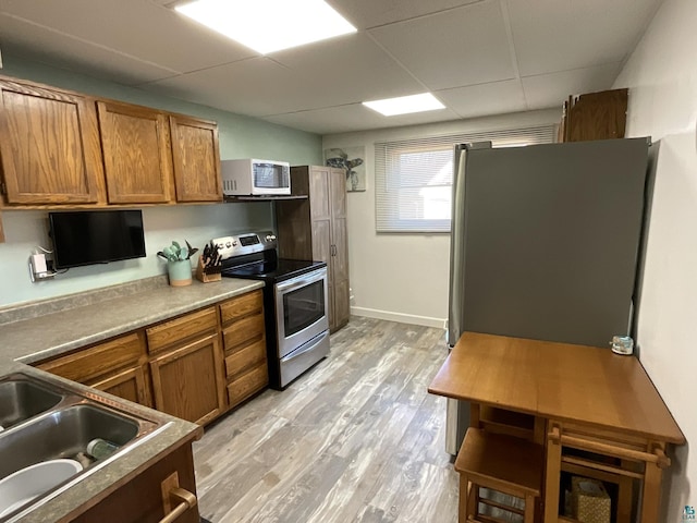 kitchen with light wood finished floors, a drop ceiling, a sink, appliances with stainless steel finishes, and brown cabinets