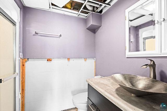 bathroom with vanity, tile walls, toilet, and a wainscoted wall