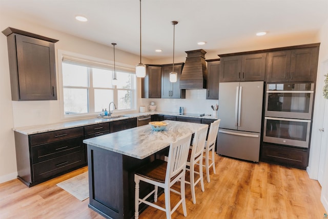 kitchen with premium range hood, a kitchen bar, a sink, stainless steel appliances, and dark brown cabinets