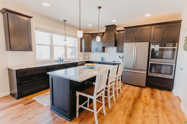 kitchen featuring a sink, a kitchen breakfast bar, appliances with stainless steel finishes, custom exhaust hood, and dark brown cabinets