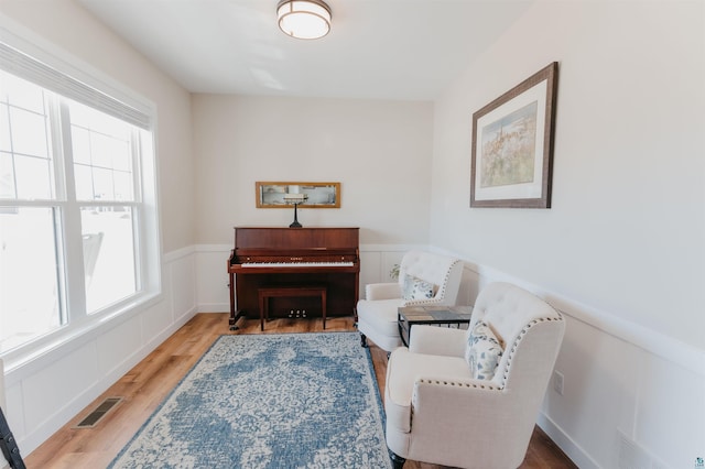 living area featuring visible vents, wainscoting, a decorative wall, and wood finished floors