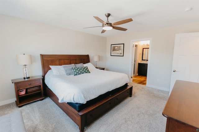 bedroom featuring light colored carpet, a ceiling fan, ensuite bathroom, and baseboards