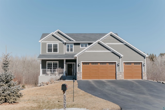 craftsman inspired home with stone siding, covered porch, driveway, and roof with shingles