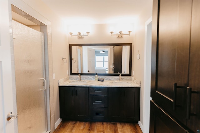 full bathroom with a sink, double vanity, wood finished floors, and a shower stall