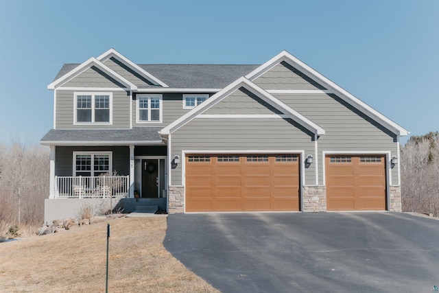 craftsman house featuring aphalt driveway, covered porch, stone siding, and roof with shingles