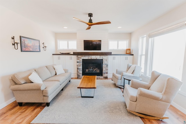 living area featuring a stone fireplace, a healthy amount of sunlight, baseboards, and light wood-style floors