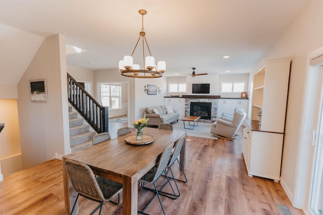 dining area with a stone fireplace, stairway, a wealth of natural light, and light wood finished floors