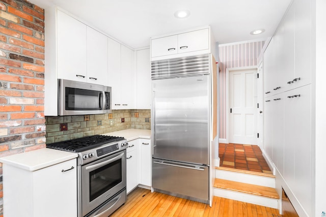 kitchen featuring light wood finished floors, decorative backsplash, stainless steel appliances, and light countertops