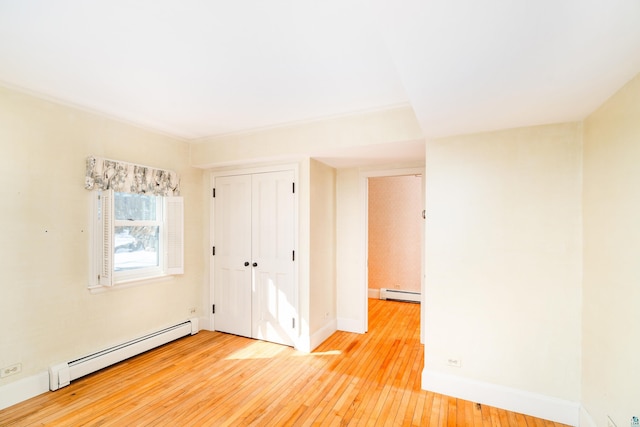 unfurnished bedroom featuring a closet, baseboards, baseboard heating, and light wood-style flooring