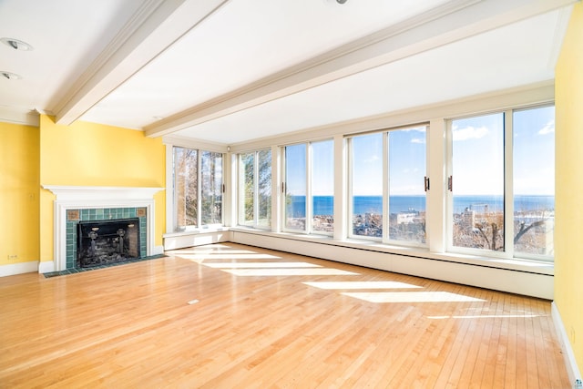 unfurnished living room with crown molding, baseboards, beamed ceiling, a tile fireplace, and wood finished floors