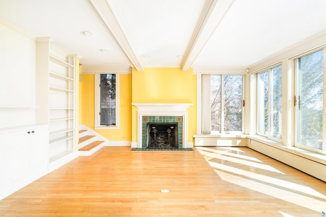 unfurnished living room with beamed ceiling, ornamental molding, a tiled fireplace, wood finished floors, and stairs