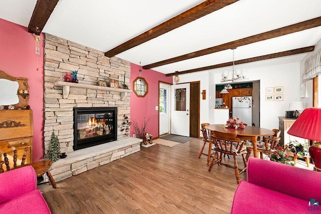 living room featuring baseboards, beamed ceiling, a stone fireplace, wood finished floors, and a notable chandelier