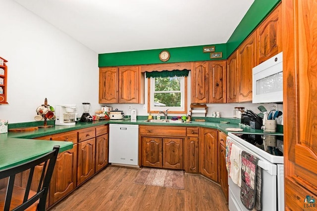 kitchen with brown cabinets, a sink, dark countertops, white appliances, and light wood finished floors