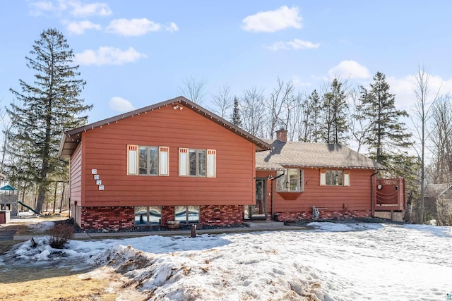 snow covered property with brick siding and a chimney