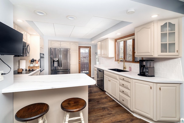 kitchen featuring a breakfast bar area, decorative backsplash, a peninsula, black appliances, and a sink