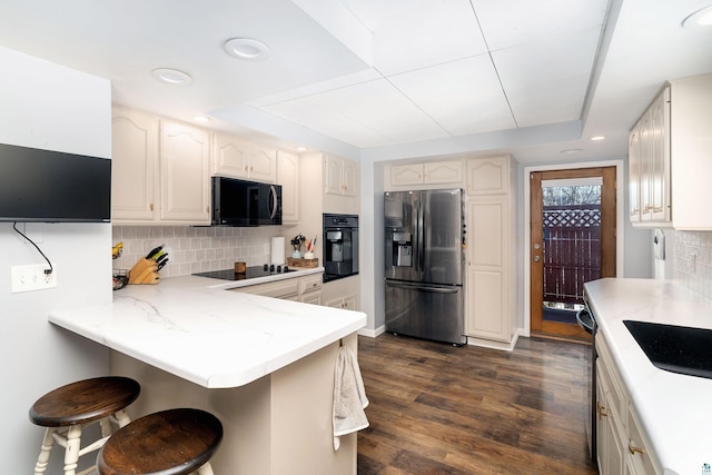 kitchen with decorative backsplash, a kitchen breakfast bar, a peninsula, black appliances, and dark wood-style flooring