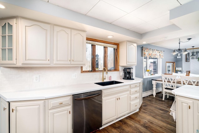 kitchen with dark wood-type flooring, a sink, a tray ceiling, stainless steel dishwasher, and decorative backsplash