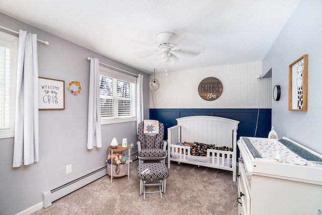 bedroom featuring baseboards, carpet floors, ceiling fan, a nursery area, and a baseboard heating unit