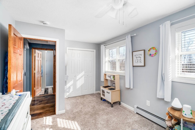 bedroom featuring a baseboard heating unit, multiple windows, baseboards, and a closet