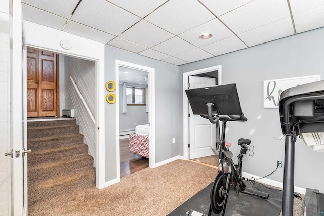 exercise area featuring a drop ceiling, baseboards, carpet floors, and a baseboard heating unit