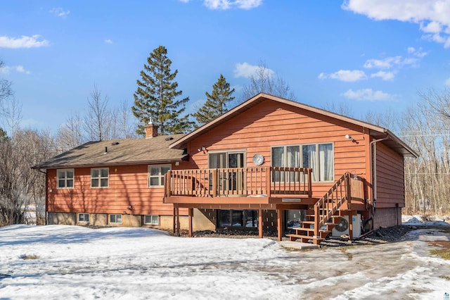 snow covered back of property with a deck, ac unit, cooling unit, and a chimney