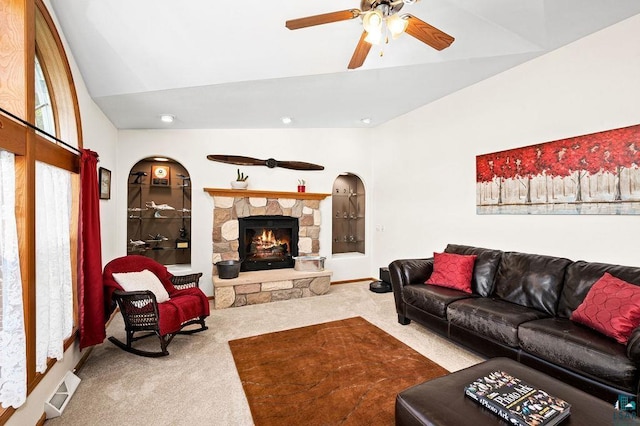 carpeted living area featuring built in shelves, visible vents, lofted ceiling, ceiling fan, and a stone fireplace