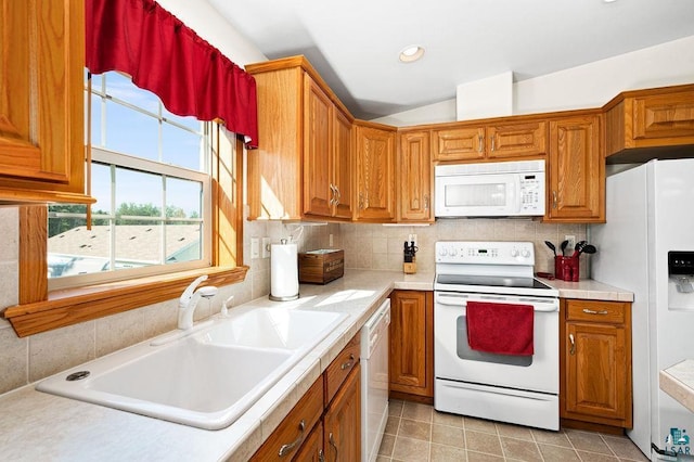 kitchen featuring backsplash, light countertops, brown cabinets, white appliances, and a sink