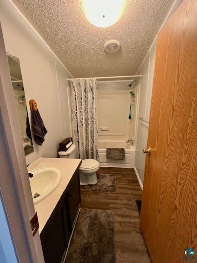 full bath with shower / tub combo with curtain, toilet, a textured ceiling, wood finished floors, and vanity