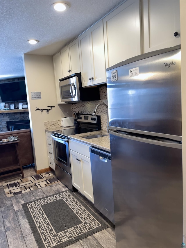 kitchen with a sink, wood finished floors, stainless steel appliances, white cabinets, and decorative backsplash