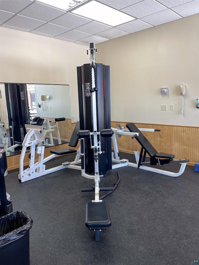 workout area with wood walls, a drop ceiling, and wainscoting