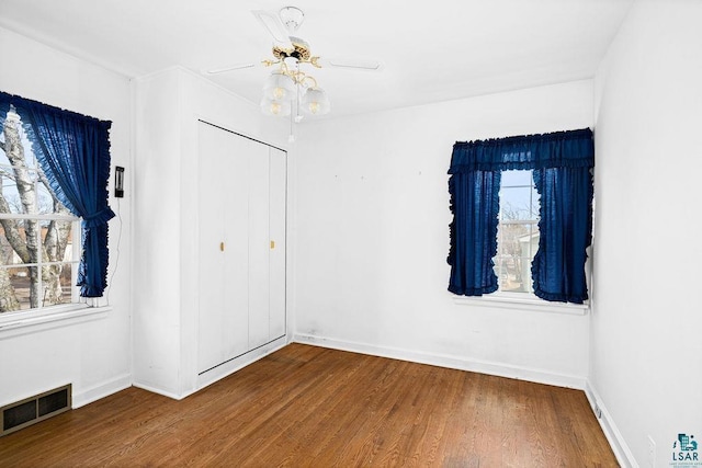 unfurnished bedroom with a closet, visible vents, multiple windows, and wood finished floors