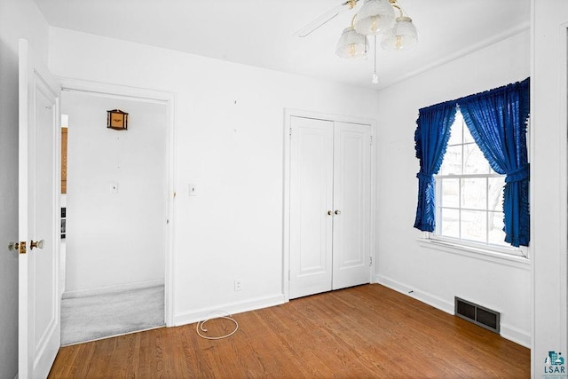 unfurnished bedroom with wood finished floors, visible vents, a closet, and baseboards