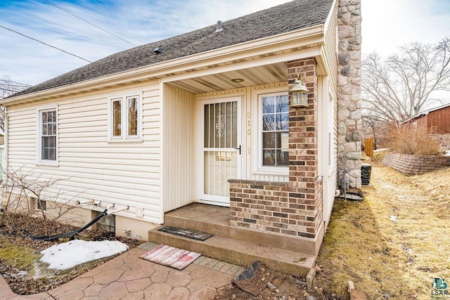 property entrance featuring brick siding, roof with shingles, and a chimney