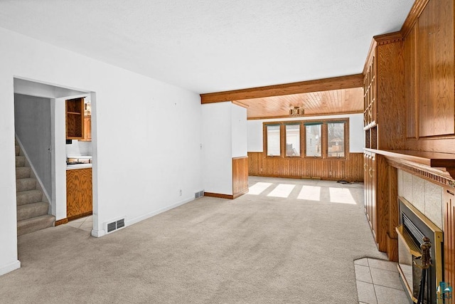 unfurnished living room featuring visible vents, a wainscoted wall, wooden walls, light colored carpet, and stairs