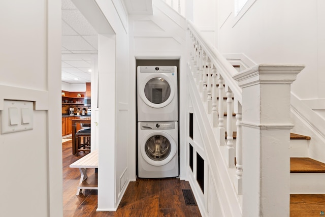 washroom with visible vents, stacked washer and dryer, dark wood-style floors, and laundry area