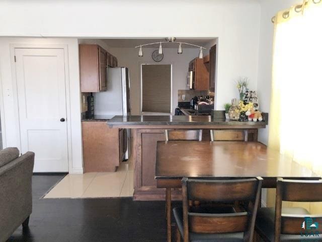 kitchen with brown cabinets, backsplash, dark countertops, stainless steel appliances, and a peninsula