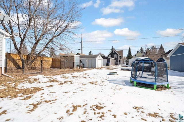 snowy yard featuring an outbuilding, a trampoline, fence, a residential view, and a storage shed