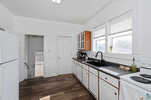 kitchen with a sink, plenty of natural light, dark countertops, dark wood-style floors, and white appliances