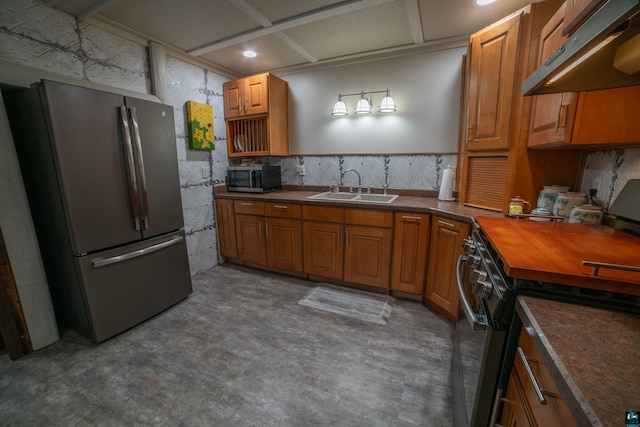 kitchen with under cabinet range hood, brown cabinets, appliances with stainless steel finishes, and a sink