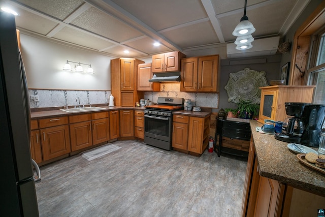 kitchen with brown cabinets, under cabinet range hood, a sink, freestanding refrigerator, and stainless steel range with gas cooktop