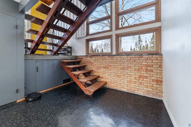 stairway with tile patterned floors, baseboards, brick wall, and a towering ceiling