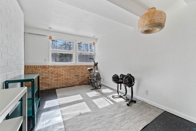 exercise room featuring baseboards and brick wall