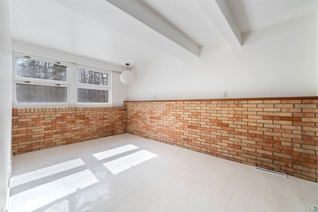 unfurnished room with visible vents, brick wall, beam ceiling, wainscoting, and tile patterned floors