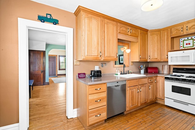 kitchen featuring light countertops, light wood-style flooring, arched walkways, white appliances, and a sink