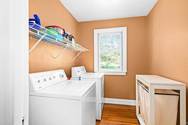 clothes washing area featuring laundry area, wood finished floors, washing machine and dryer, and baseboards